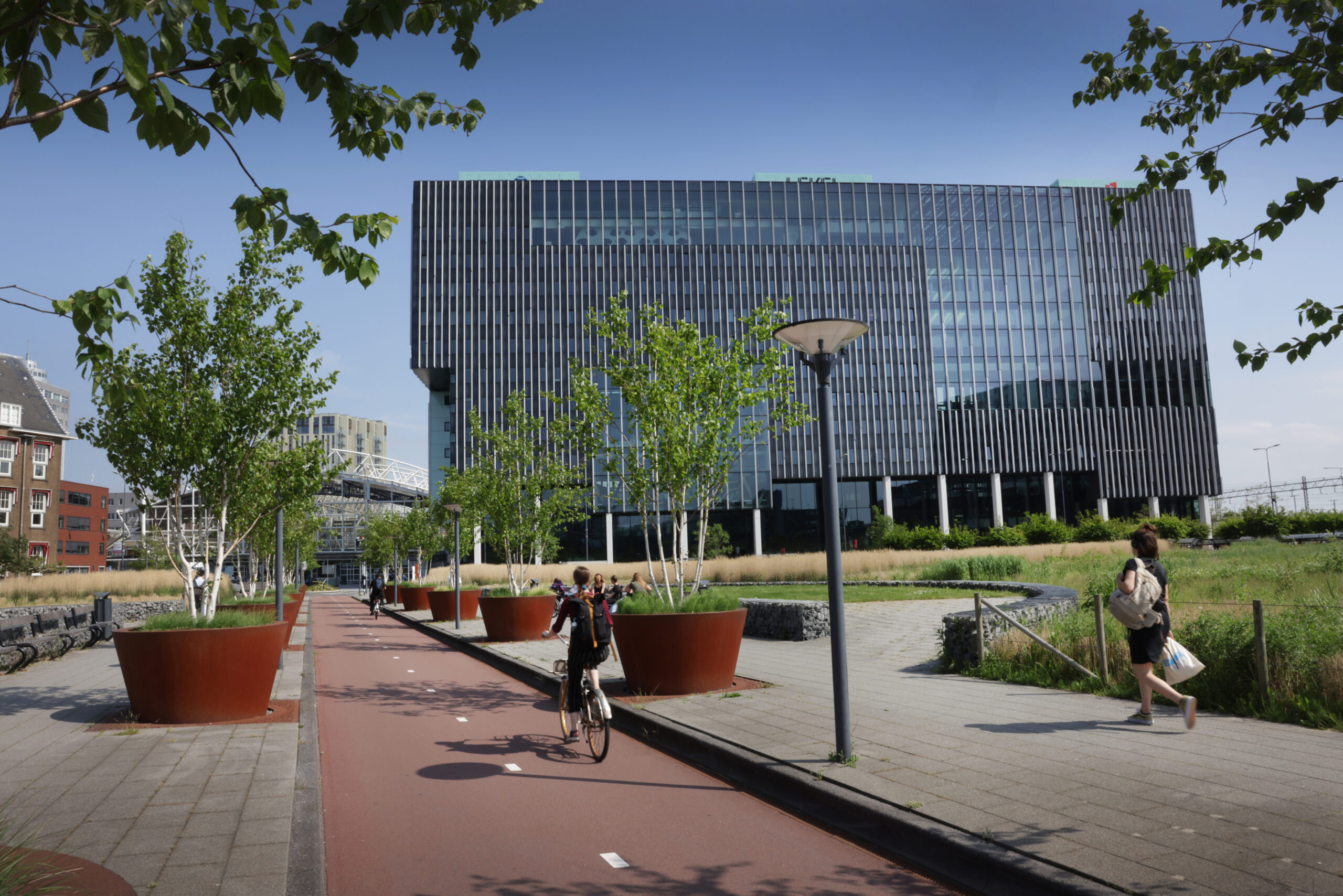 Moderne glazen gevel van gebouw x2X4A8680 met omliggende fietspaden en groenvoorzieningen.