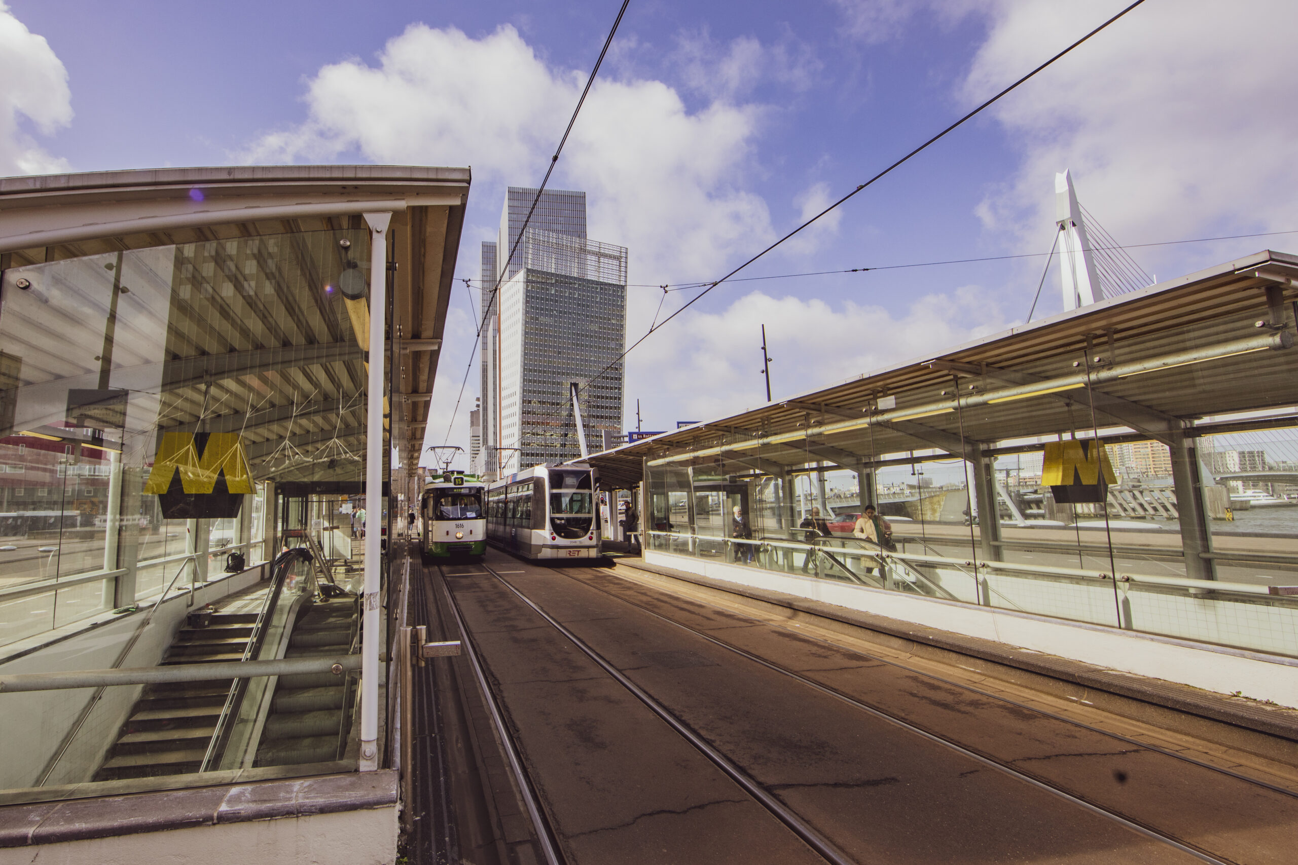 Tramhalte in Rotterdam met zicht op de Erasmusbrug en moderne kantoorgebouwen.