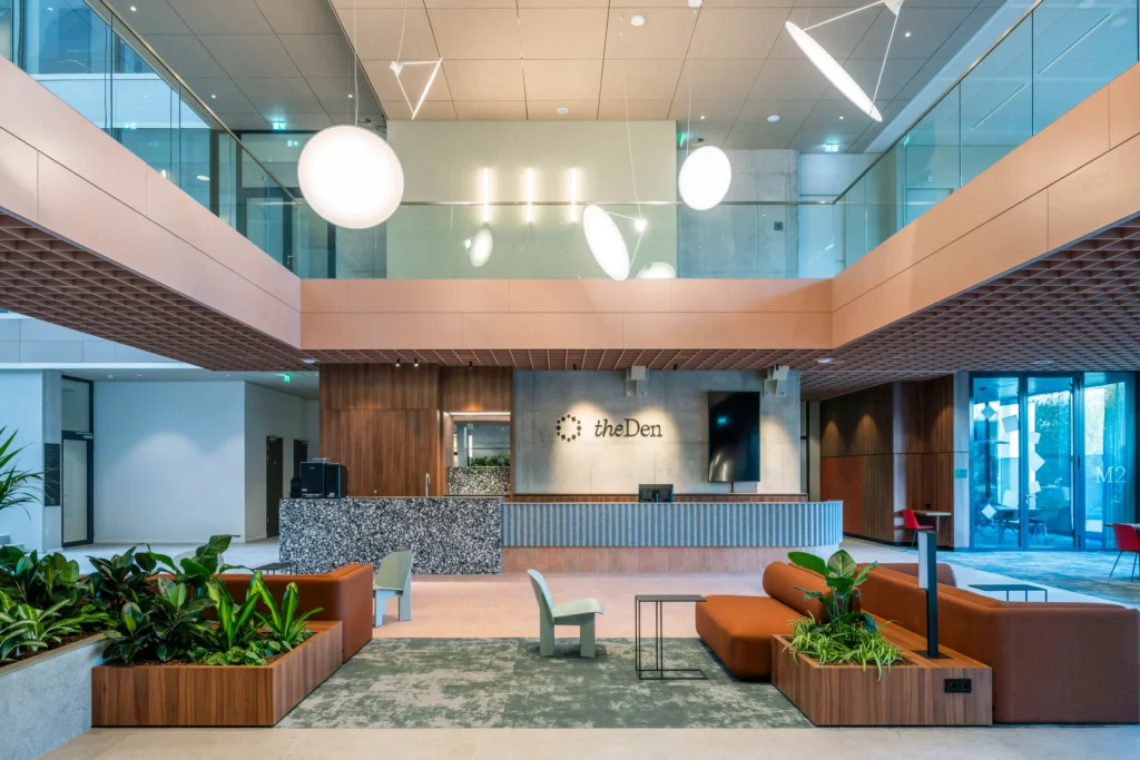 Moderne hotellobby van The Den met een chique receptiebalie, designmeubels en veel groen.