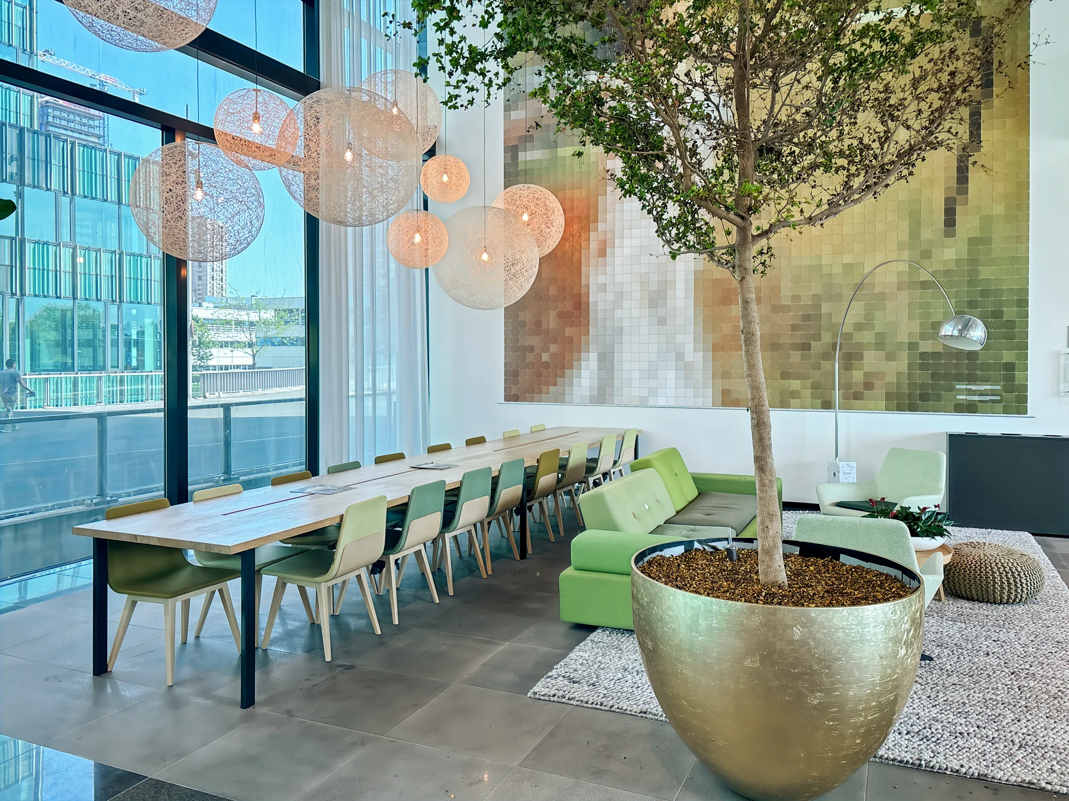 Een moderne kantoorruimte met een lange vergadertafel, veel groen en grote decoratieve lampen.