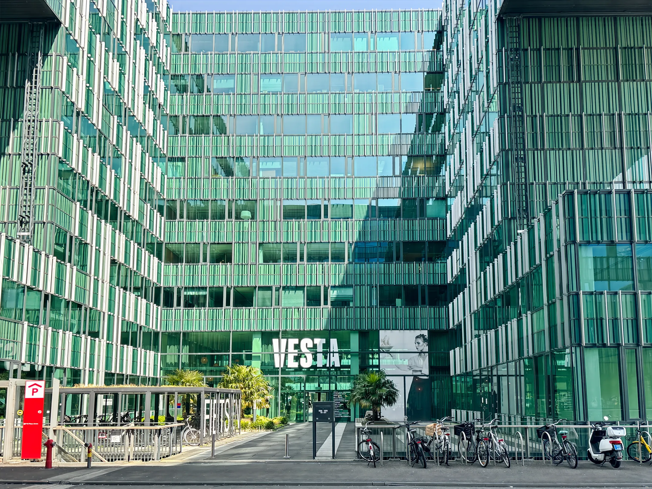 Een modern kantoorgebouw met glazen gevels genaamd VESTA en fietsenrekken aan de voorkant.