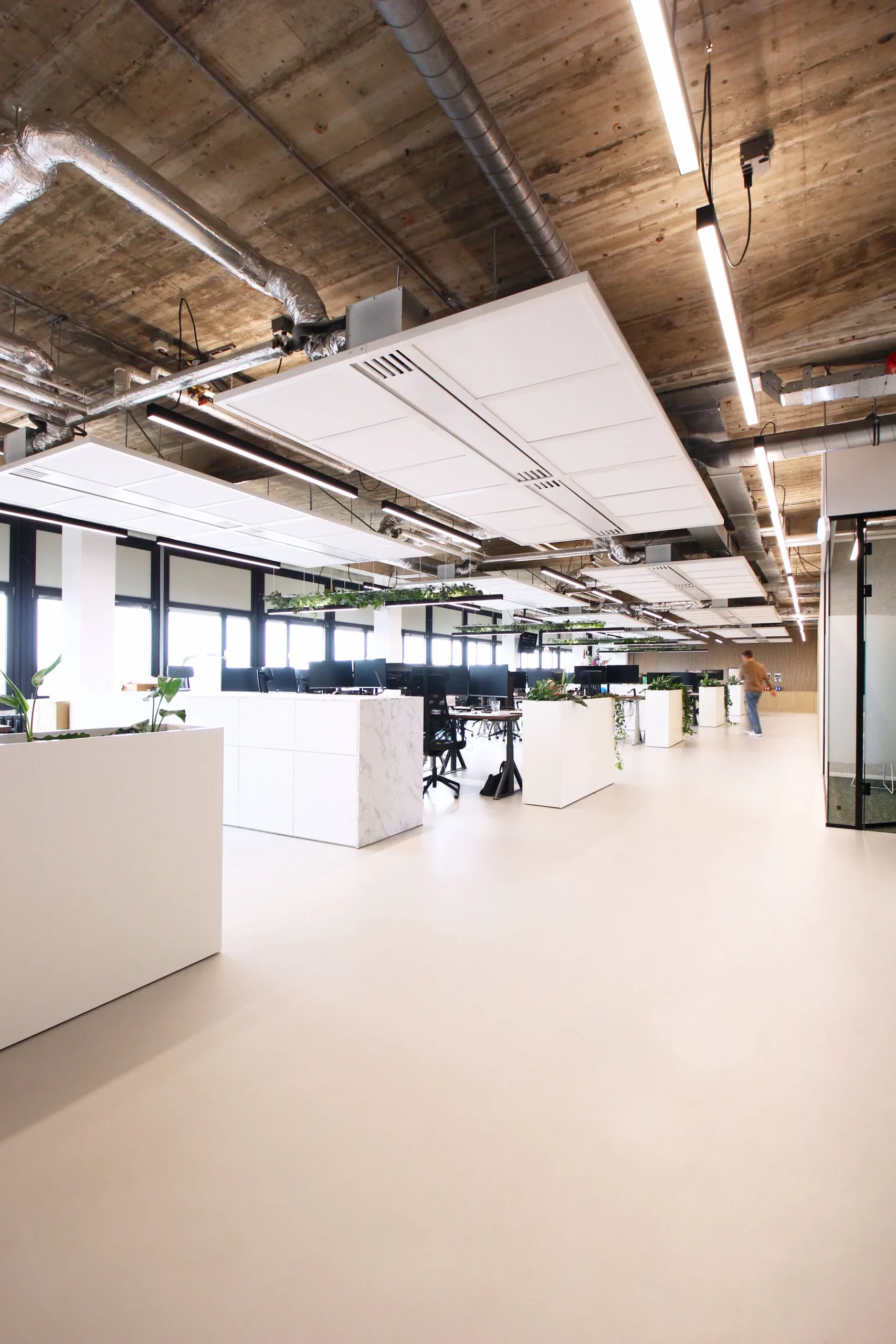 Een modern en ruim kantoor met open werkplekken, planten en een industrieel plafond.