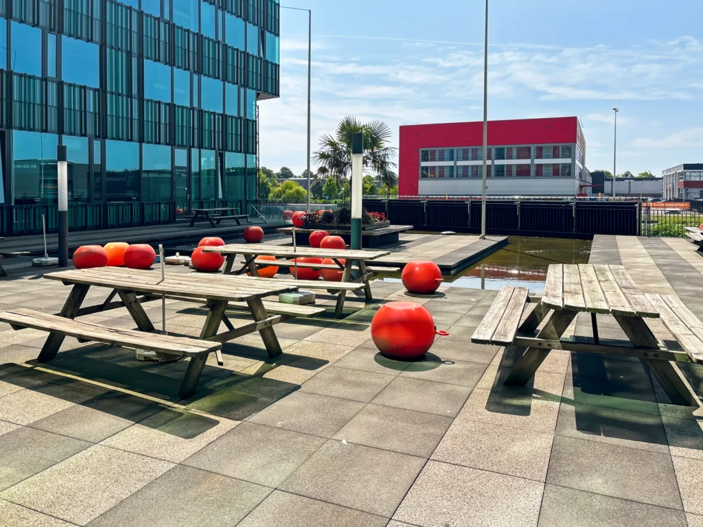 Zonovergoten dakterras met picknicktafels en rode ballen naast een modern gebouw.