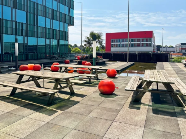 Zonovergoten dakterras met picknicktafels en rode ballen naast een modern gebouw.