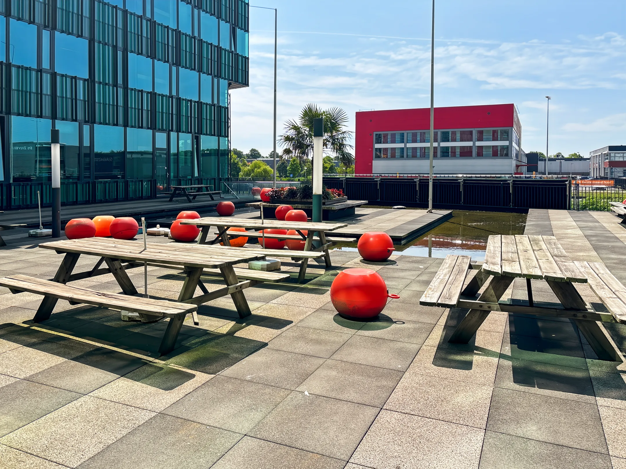 Zonovergoten dakterras met picknicktafels en rode ballen naast een modern gebouw.
