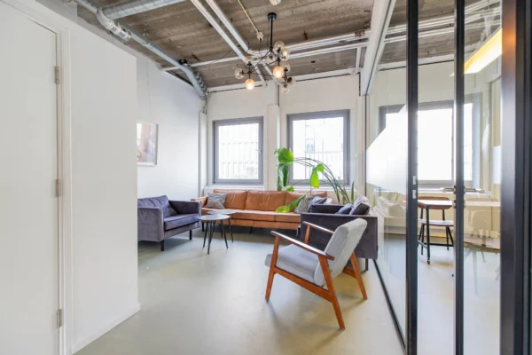 Een moderne, lichte woonkamer met een bruine bank, grijze stoelen en kamerplant in het midden.