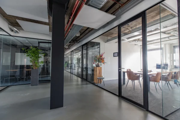 Een moderne kantoorruimte met glazen wanden, planten en vergadertafels.