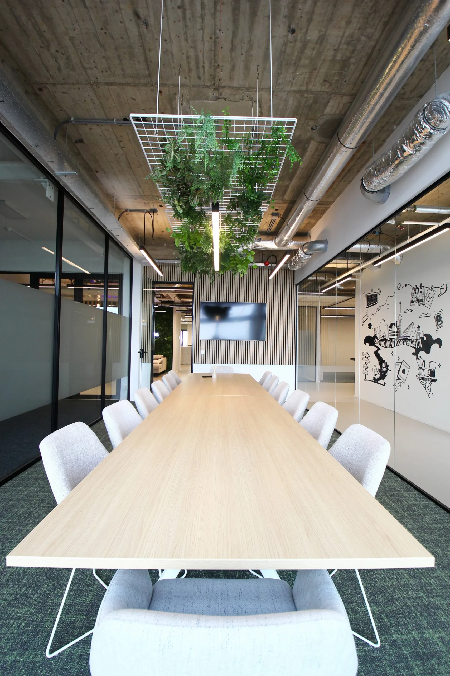 Een moderne vergaderruimte met een lange houten tafel, stoelen, hangende plantdecoratie en een muurschildering.