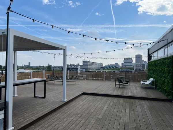 Rooftopterras met pergola, tafels, stoelen en uitzicht op de stad.