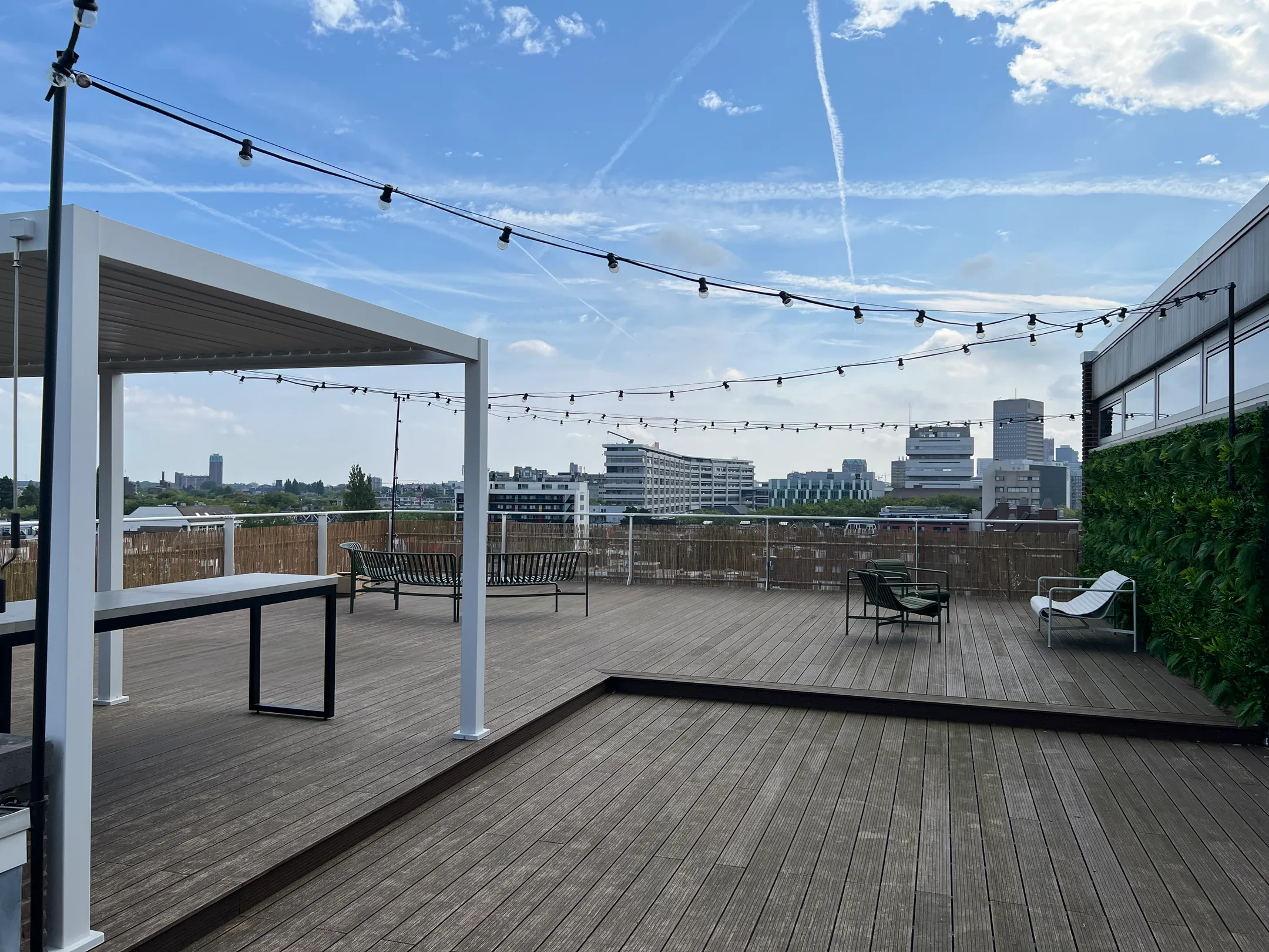 Rooftopterras met pergola, tafels, stoelen en uitzicht op de stad.