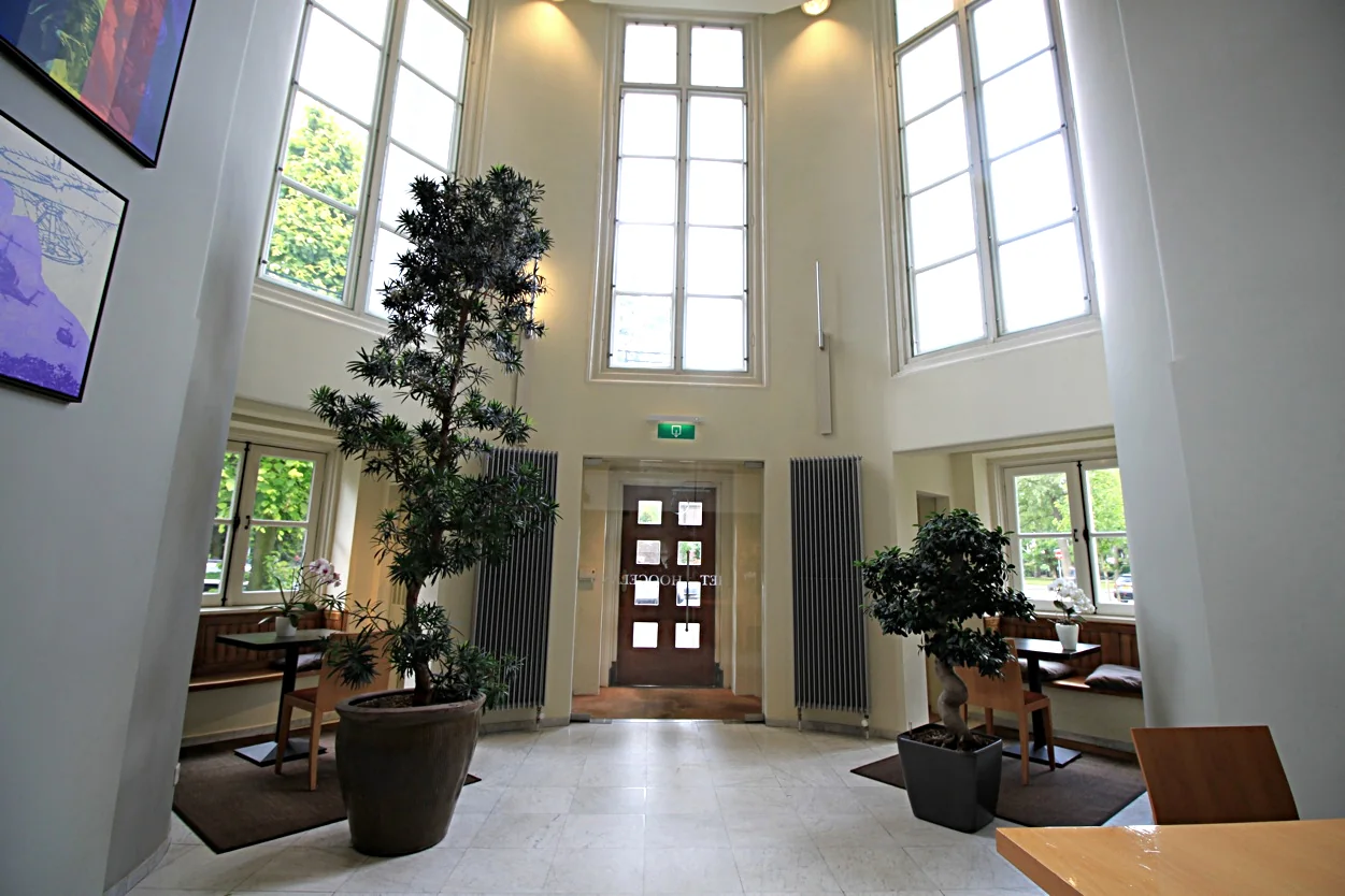 Lichte en hoge entreehal van Museumlaan 39343675 met grote ramen, planten en zitplekken bij de ramen.