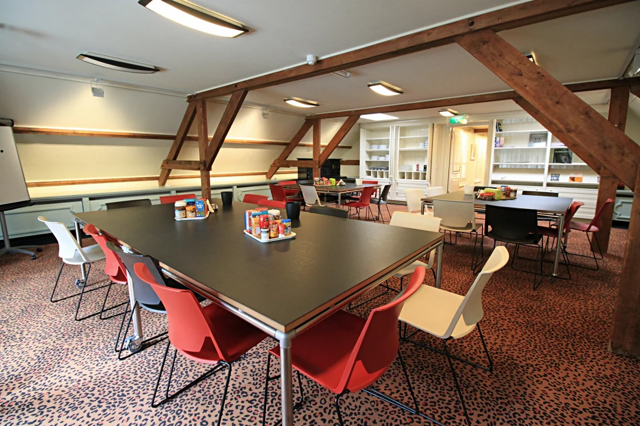 Vergaderruimte met moderne tafels, kleurrijke stoelen en houten balken, gelegen aan de Museumlaan.