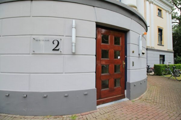 Ingang van een statig gebouw aan de Museumlaan 2 met houten deur en gevelbord.