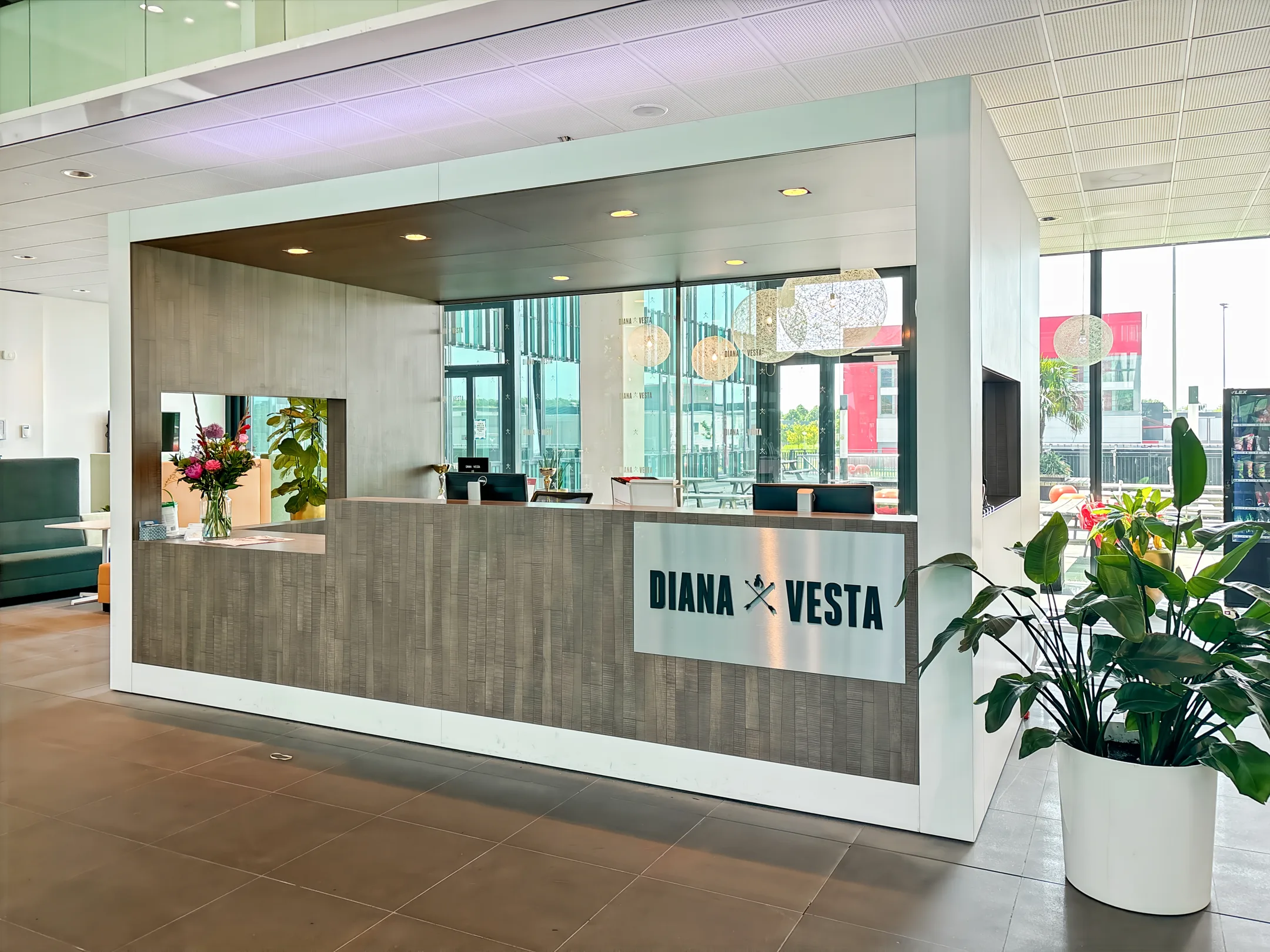 Een moderne receptiebalie van Diana Vesta met bloemen en planten in een lichte, glazen ruimte.