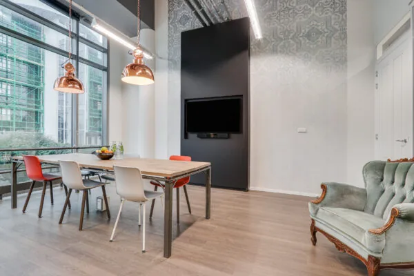 Modern vergadergedeelte in Den Haag met houten tafel, kleurrijke stoelen, een flatscreen en industriële accenten.