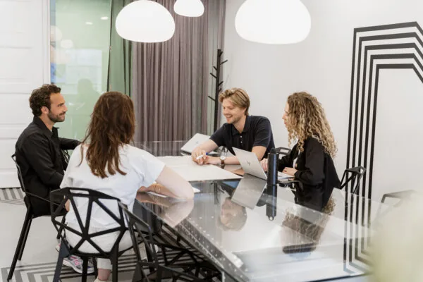 Vier mensen overleggen aan een glazen vergadertafel in een moderne ruimte bij HNK Amsterdam Schinkel.