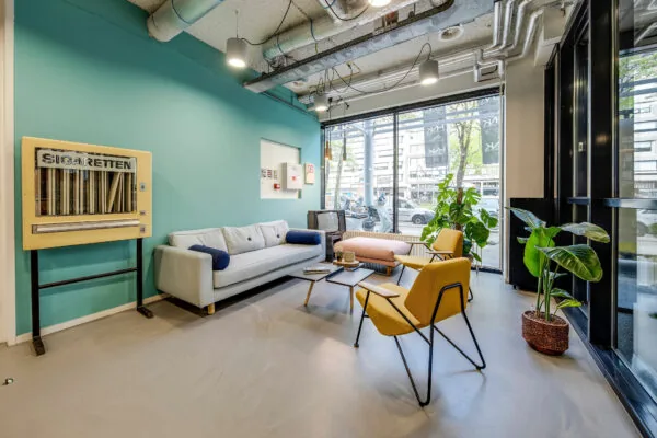 Moderne loungehoek in HNK Rotterdam Centrum met vintage sigarettenautomaat, zitbanken en kamerplanten.