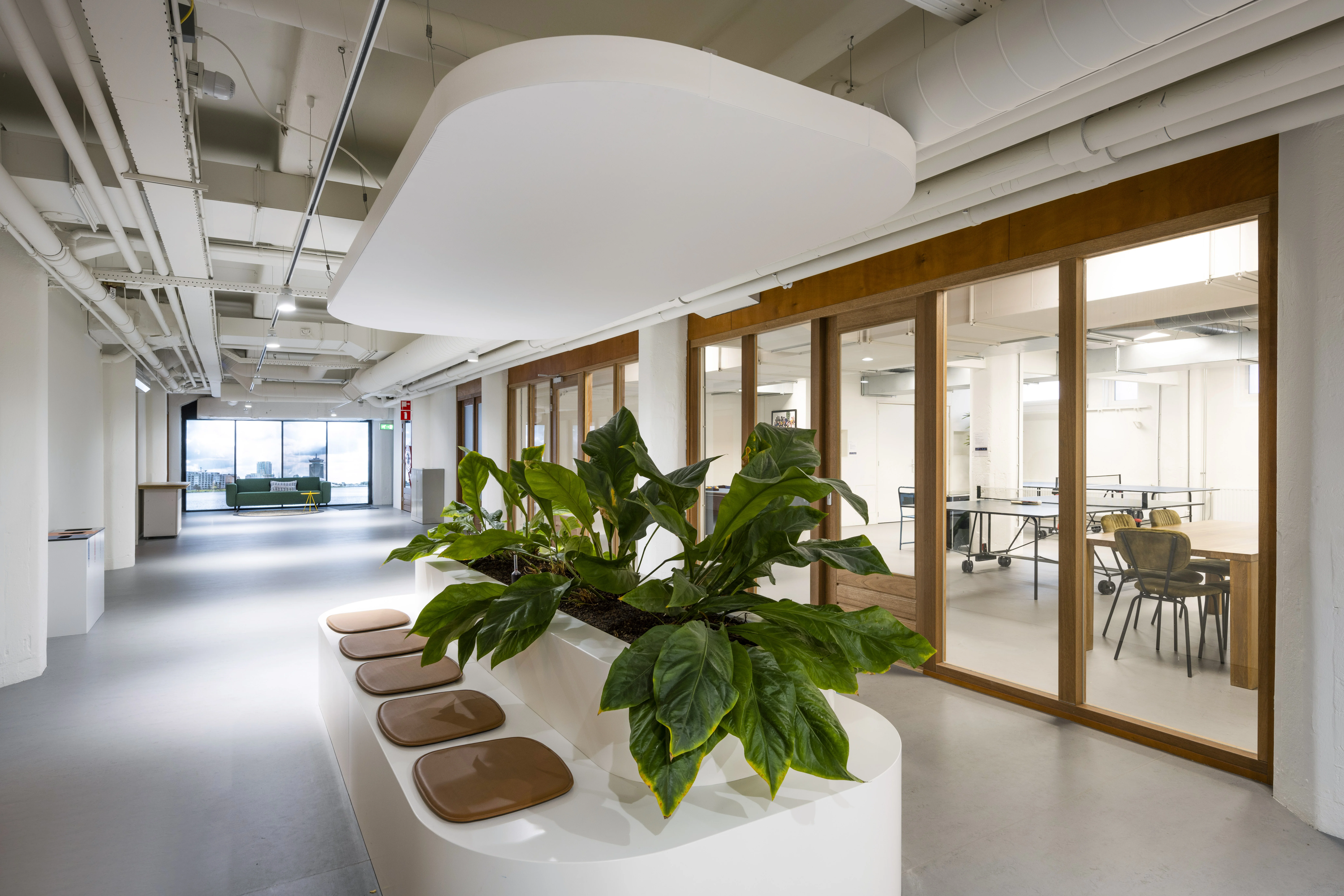 Moderne kantoorruimte in HNK Diemen met een ovale zitbank met planten en zicht op vergaderruimtes met glazen wanden.