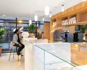 Moderne koffiecorner in kantoorruimte Schimmelt 2-16 in Eindhoven met mensen in gesprek en koffieautomaten op de achtergrond.