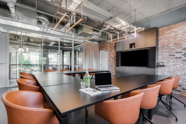 Moderne vergaderruimte in Utrecht Centraal met zwarte tafel, leren stoelen, een tv-scherm en industriële plafondafwerking.