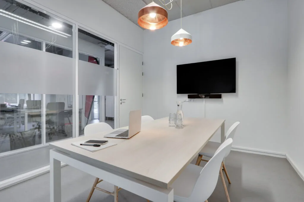 Moderne vergaderruimte in Utrecht West met witte inrichting, een houten tafel, laptop en wandbeeldscherm.