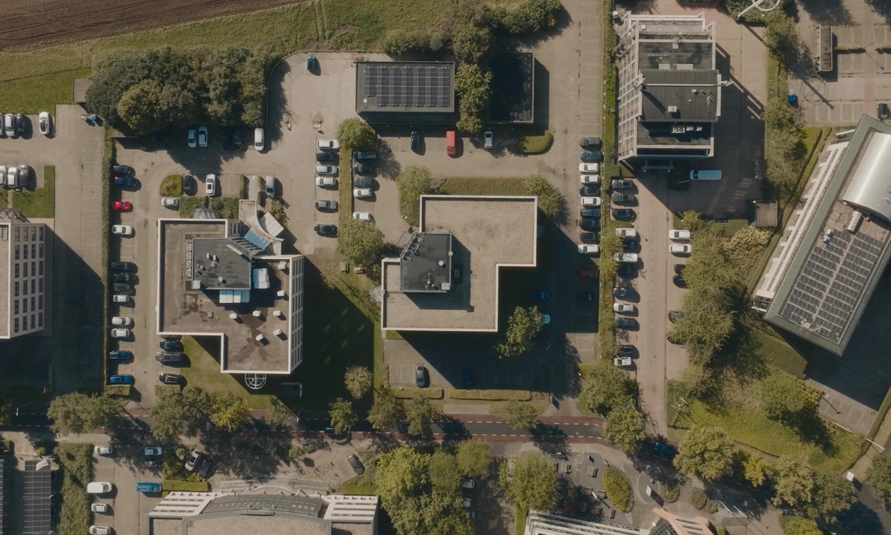 Luchtfoto van een kantoorpark met meerdere gebouwen, parkeerplaatsen en groene zones.