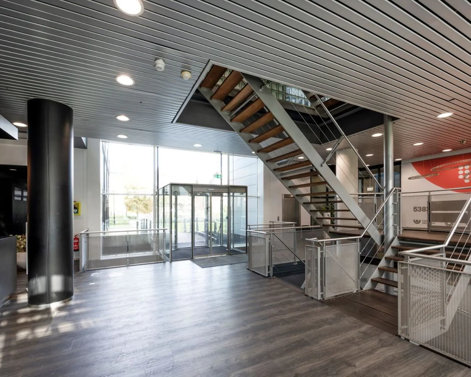 Moderne, lichte kantoorentree met houten trap en glazen draaideur aan het Rietlandpark 309-357 in Amsterdam.