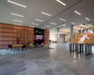Moderne en ruime kantoorlobby aan de Taurusavenue 165 in Hoofddorp met zitgedeelte, houten traptribune en glazen toegangspoortjes.