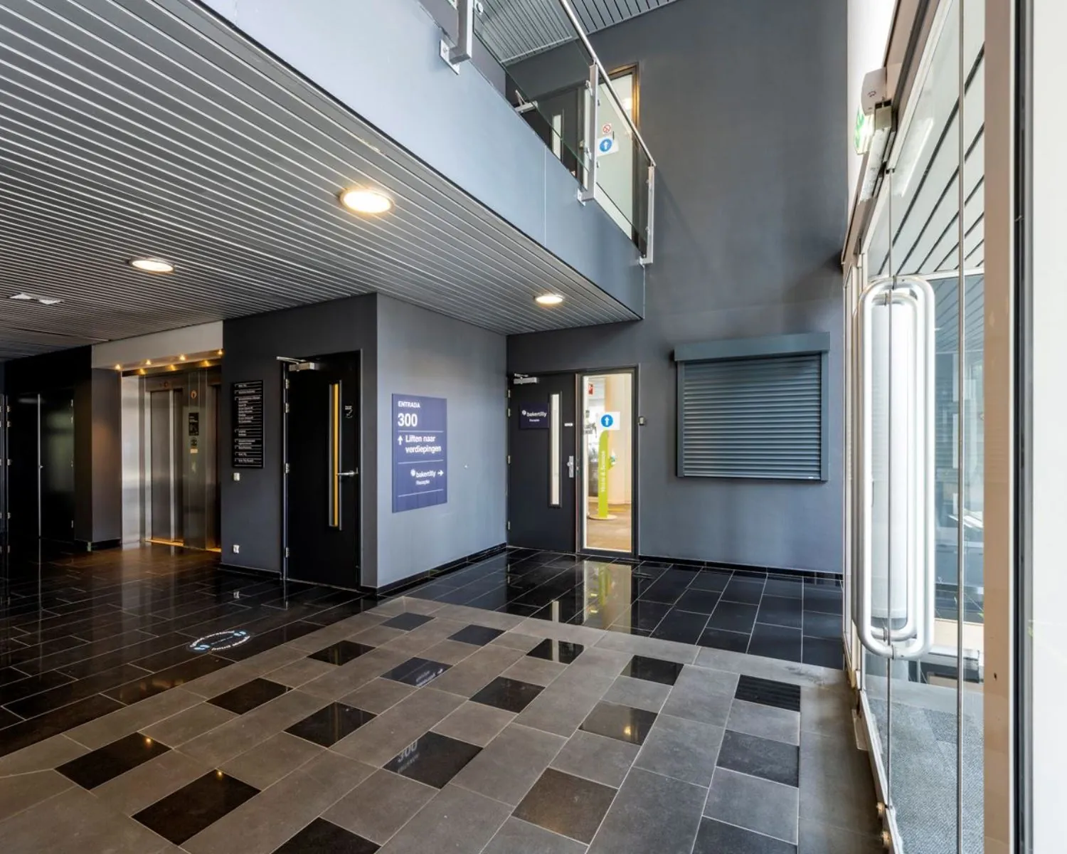 Moderne entreehal van kantoorruimte Entrada 300 in Amsterdam met lift, glazen deuren en zwart-grijze vloertegels.