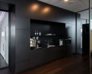 Moderne zwarte pantry met ingebouwde apparatuur in kantoorruimte aan de Herikerbergweg 292 in Amsterdam.
