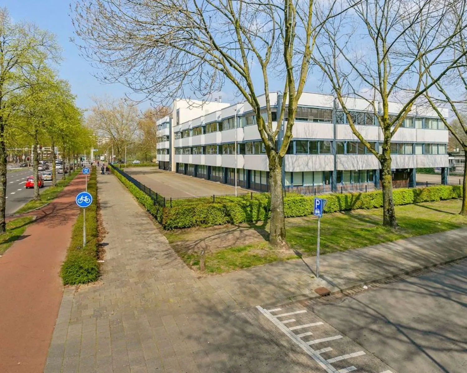 Wit kantoorgebouw aan de Hooilaan 1 in Breda met omliggend groen en fietspad langs een drukke weg.
