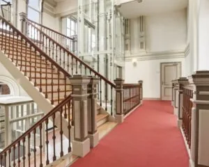 Trappenhuis met rood tapijt en glazen lift in een representatief kantoorgebouw aan de Wilhelminastraat 43a in Haarlem.
