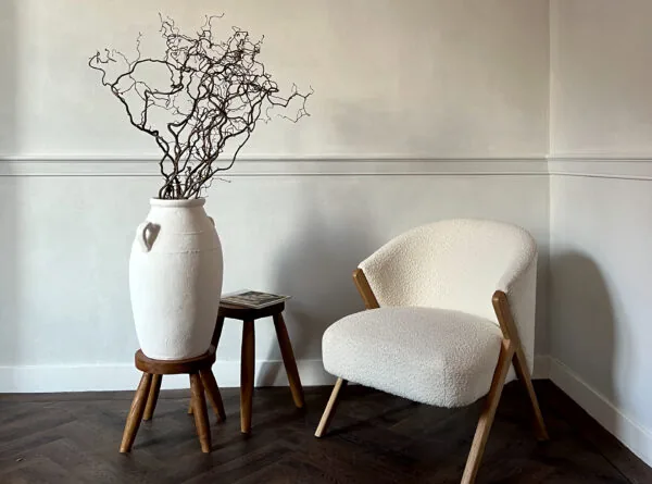 Stijlvolle minimalistische zithoek met een witte fauteuil, houten krukjes en een grote vaas met decoratieve takken bij Creativegrounds – Emmalaan.