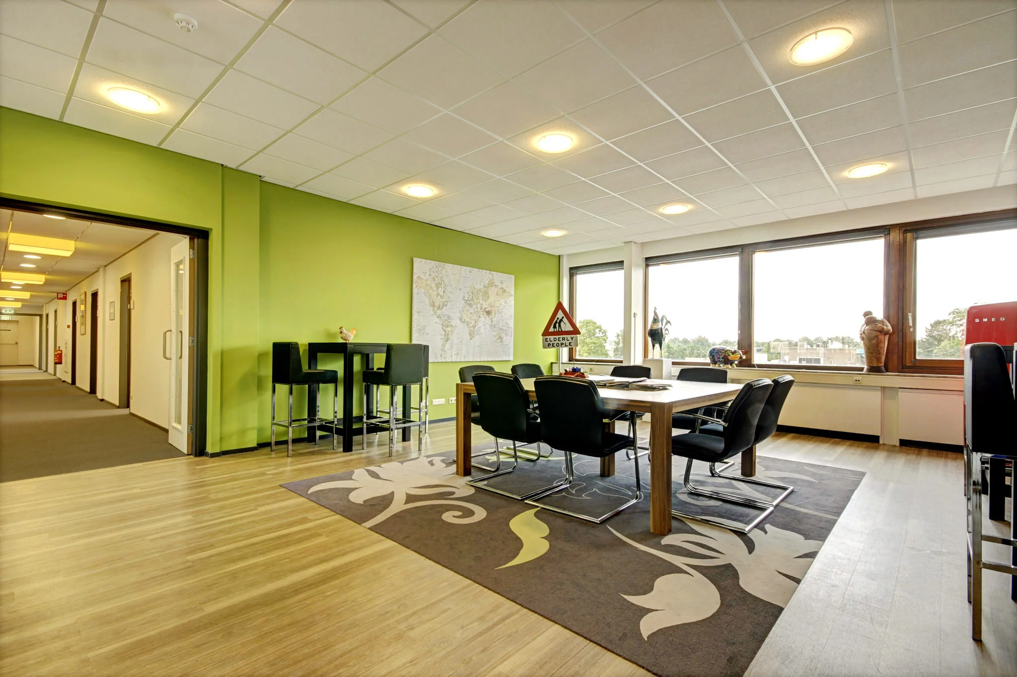 Vergaderruimte aan de Maarssenbroeksedijk met groene muur, een grote tafel, zwarte stoelen en grote ramen met uitzicht.