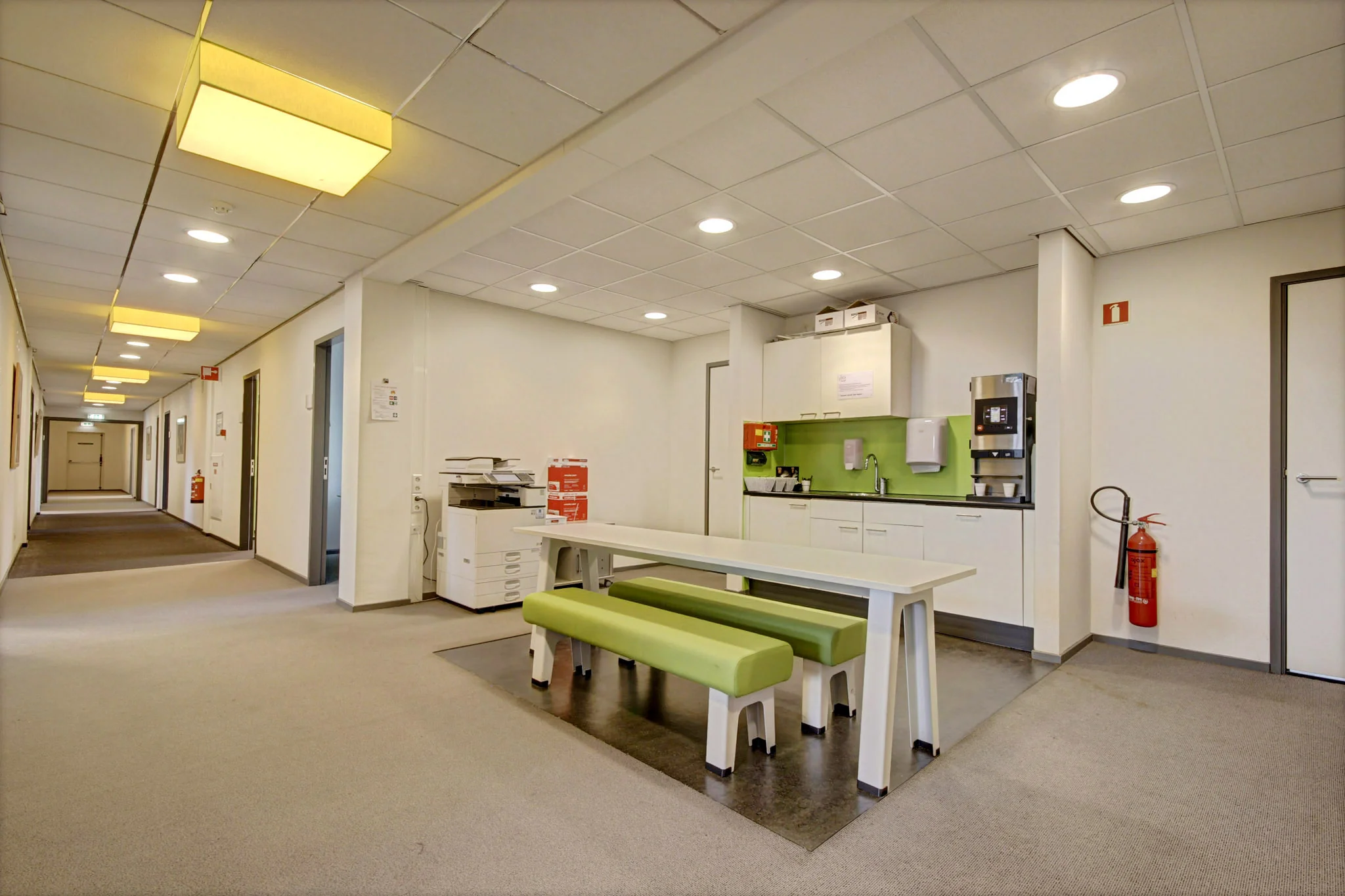 Kantinehoek met tafel, groene zitbanken en koffieautomaat in een kantoor aan de Maarssenbroeksedijk.