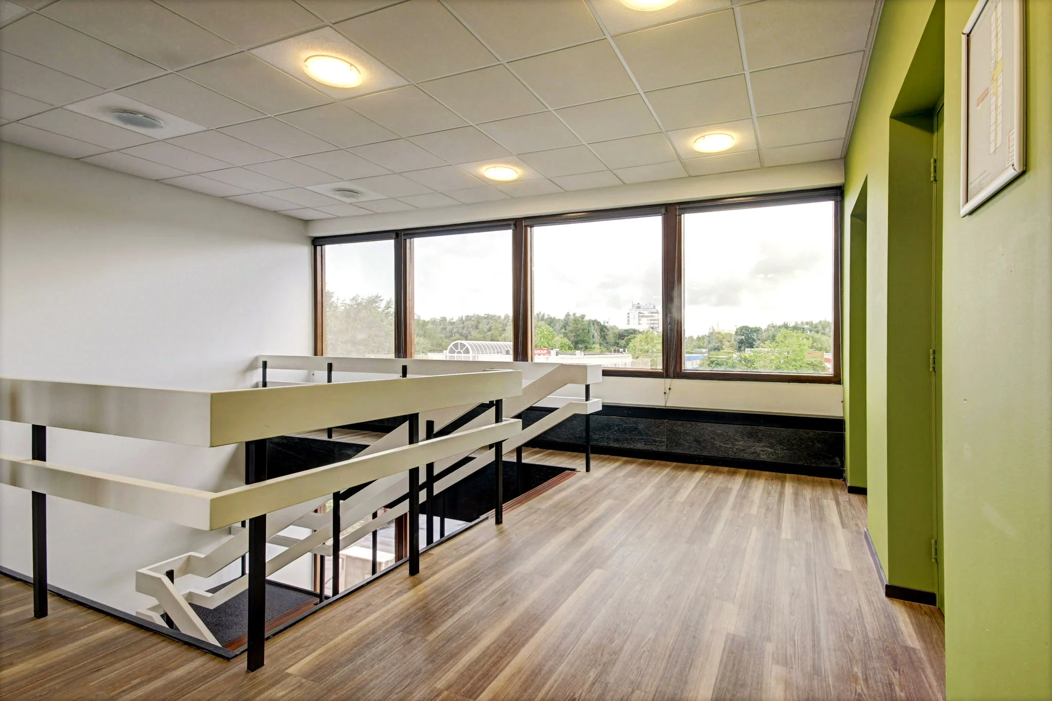 Lichte trapopgang met houten vloer en grote ramen in een gebouw aan de Maarssenbroeksedijk.