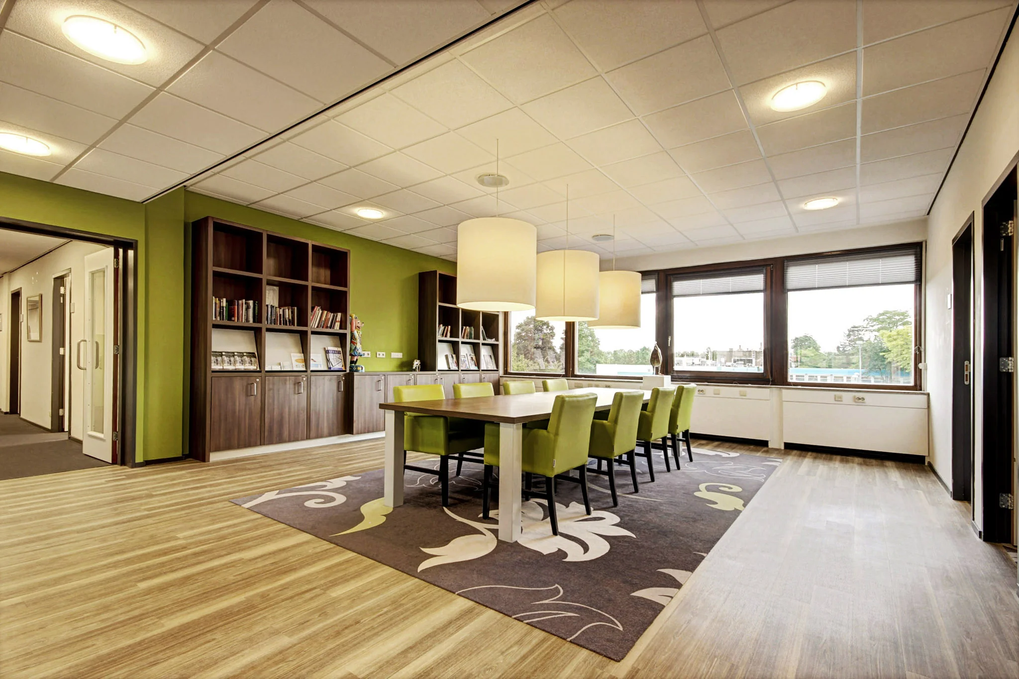 Vergaderruimte aan de Maarssenbroeksedijk met groene stoelen, houten tafel, boekenwand en grote ramen.