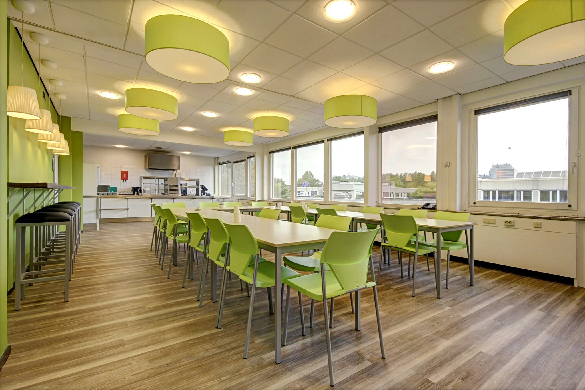 Moderne eetruimte in een bedrijfsgebouw aan de Maarssenbroeksedijk met groene stoelen, houten vloer en grote ramen.
