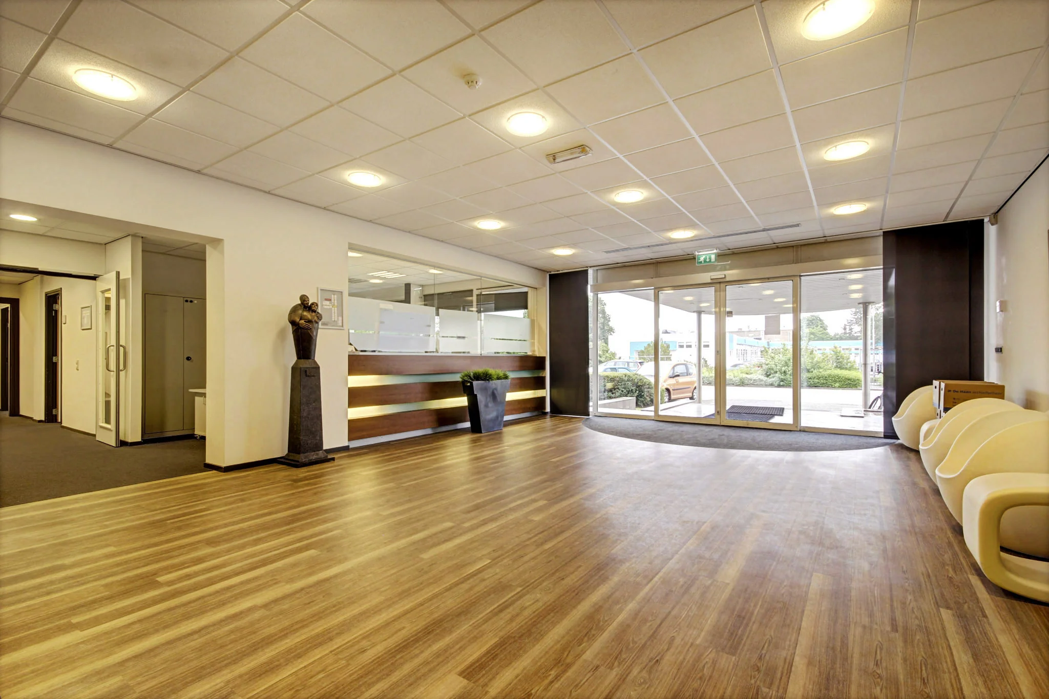 Moderne en ruime entreehal van een kantoor aan de Maarssenbroeksedijk met houten vloer, balie en glazen schuifdeuren.