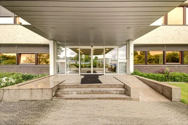 Ingang van een modern kantoorgebouw aan de Maarssenbroeksedijk met overkapping, trap en rolstoelvriendelijke oprit.
