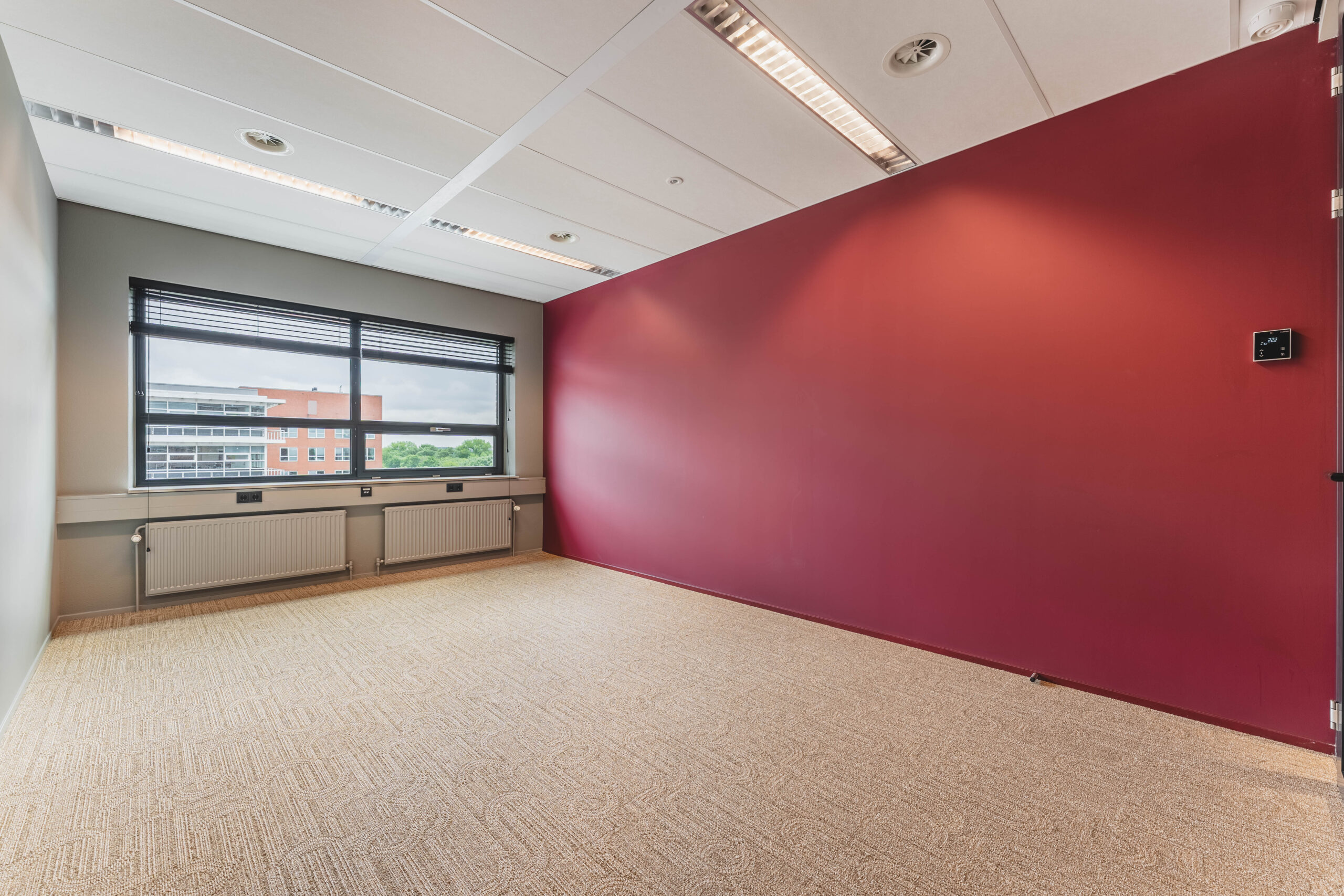 Lege kantoorruimte met een rood geverfde muur en groot raam met uitzicht naar buiten.
