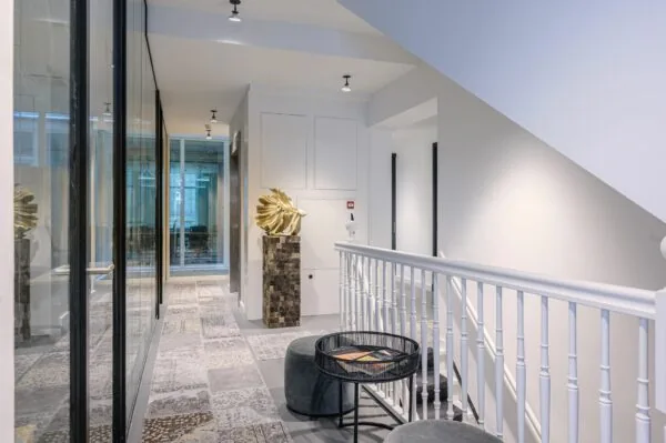 Lichte en moderne kantoorhal met glazen wanden, kunstobject en zithoekje met tafel.