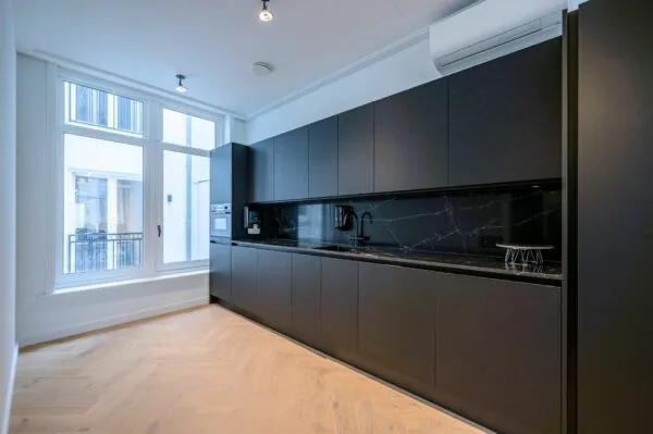 Moderne zwarte keuken met greeploze kasten, marmeren werkblad en grote ramen voor natuurlijk licht.