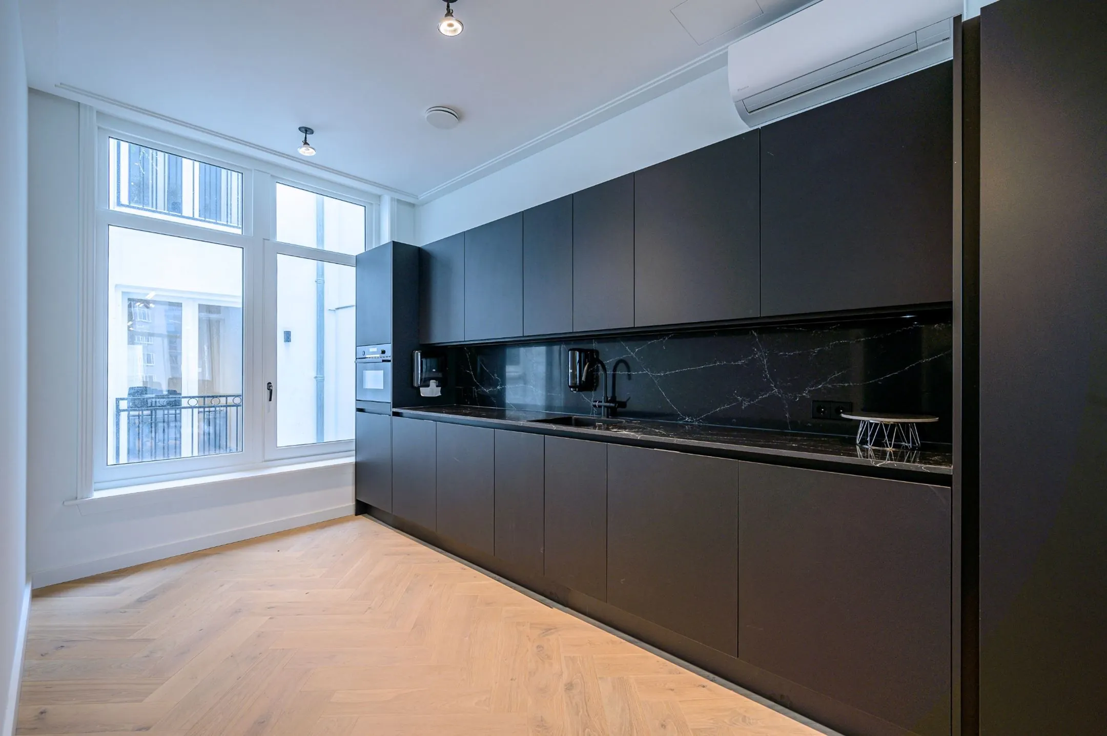 Moderne zwarte keuken met greeploze kasten, marmeren werkblad en grote ramen voor natuurlijk licht.