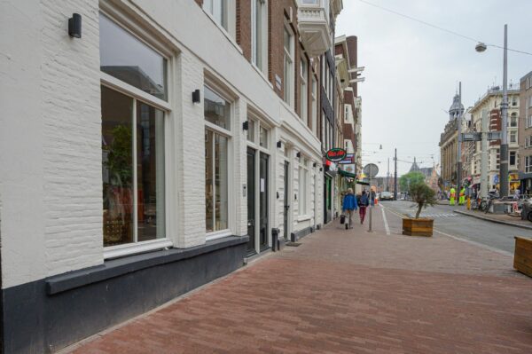 Straatbeeld van een rustige winkelstraat in Amsterdam met voetgangers, cafés en zicht op de architectuur.