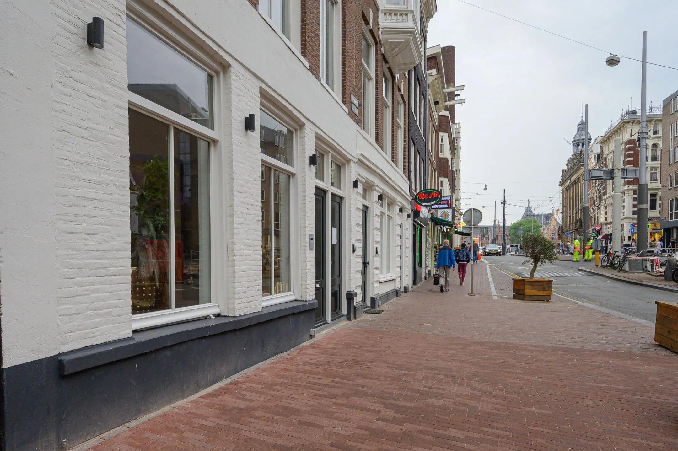 Straatbeeld van een rustige winkelstraat in Amsterdam met voetgangers, cafés en zicht op de architectuur.