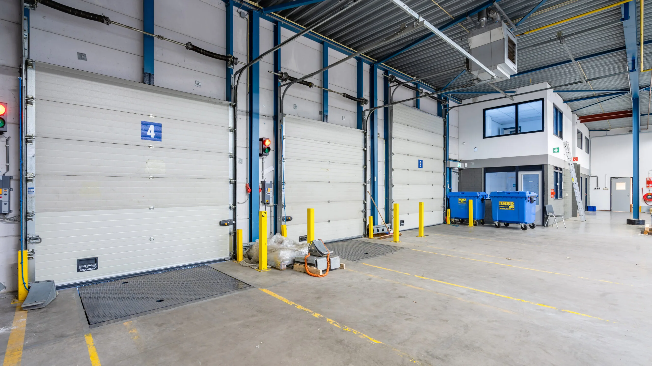 Laadperron met gesloten overheaddeuren, afvalcontainers en een kantoorruimte in een moderne logistieke loods.