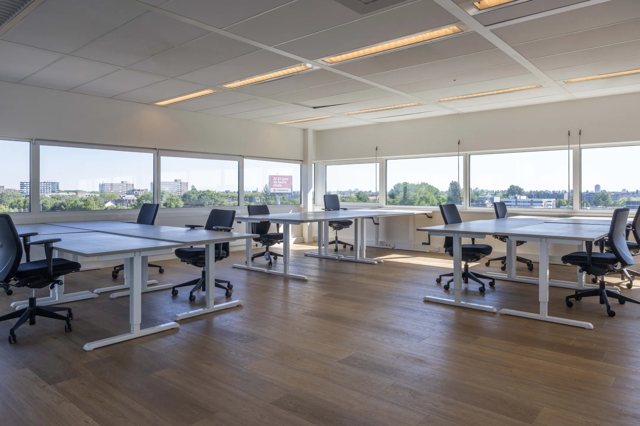 Een leeg, modern kantoor met bureaus en stoelen, omgeven door grote ramen met uitzicht op de stad.