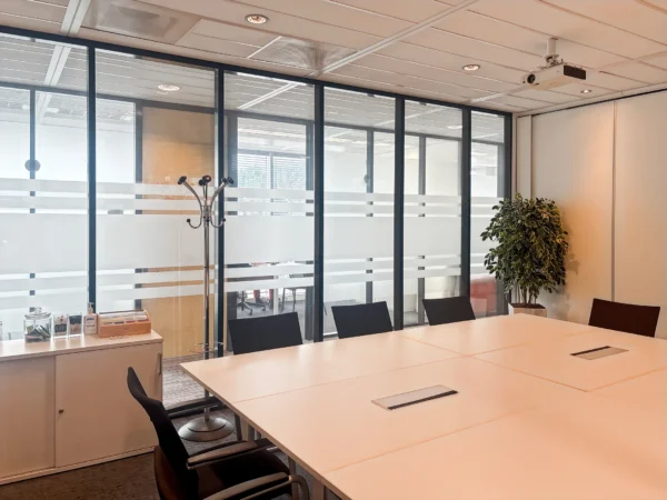 Een moderne vergaderruimte met een witte tafel, stoelen, een kapstok en een projector aan het plafond.