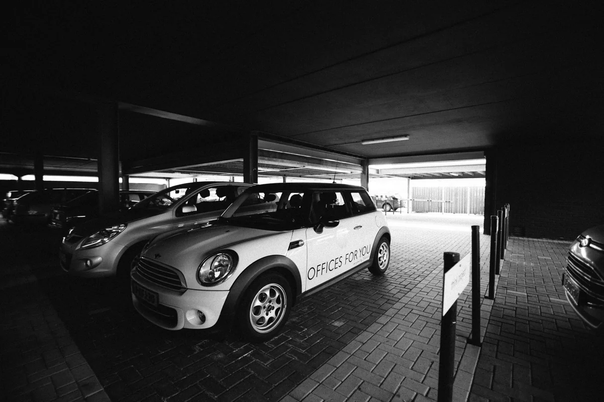 Witte Mini Cooper met "Offices for You"-opdruk geparkeerd in een overdekte parkeergarage aan de Orteliuslaan.